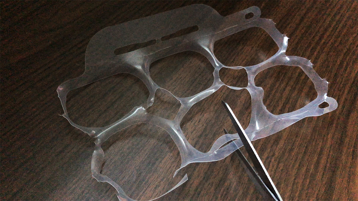 A plastic set of six-pack rings used to hold drinks together is being cut up by scissors.