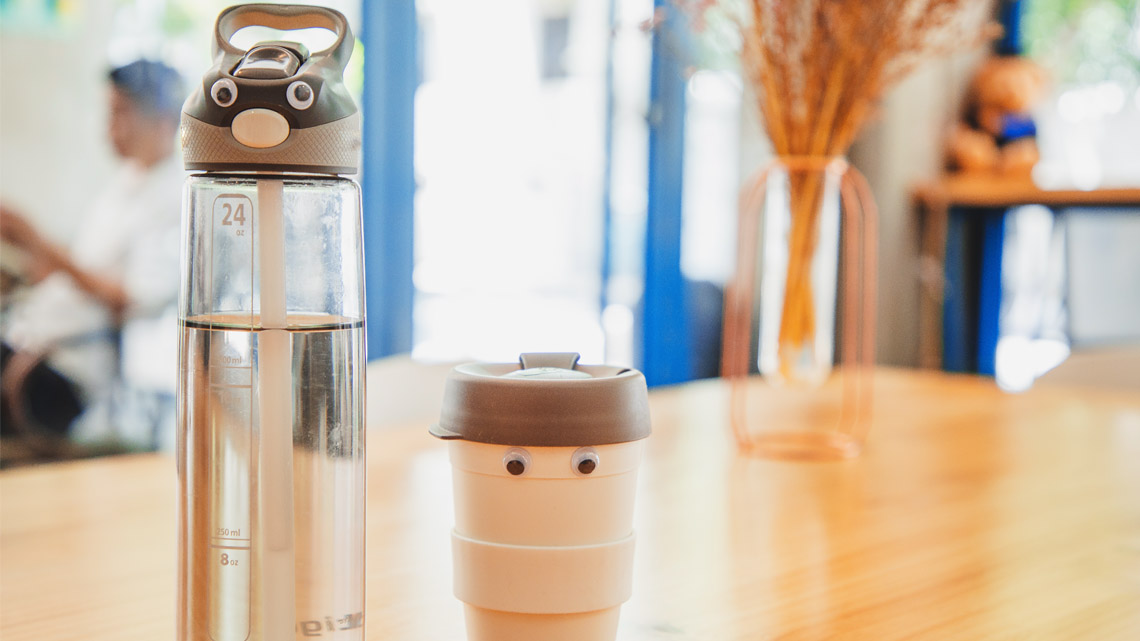 A reusable water bottle and a reusable mug are decorated with googly eyes.
