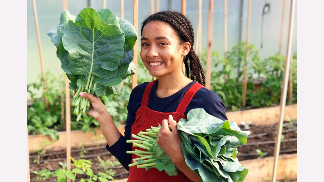 Cheyenne Sundance inside a greenhouse holding vegetables she has grown.