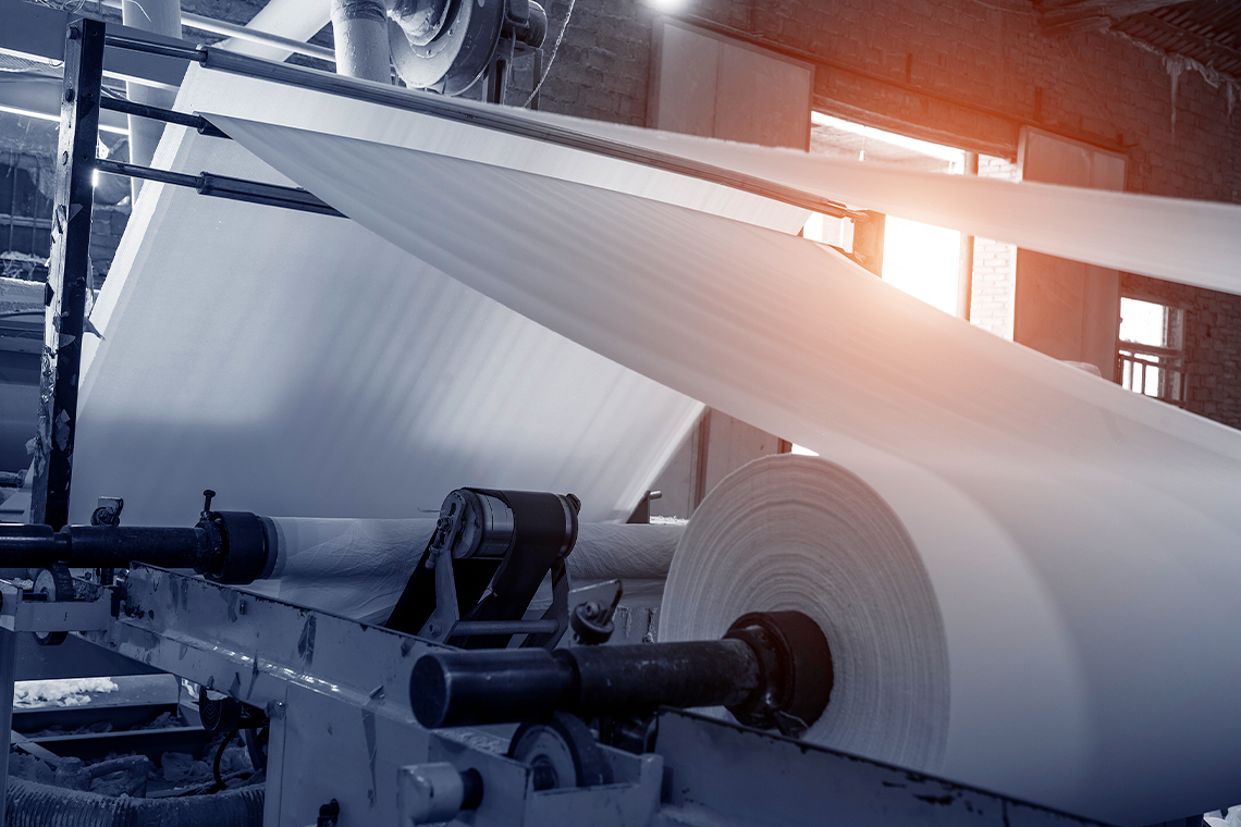 A large sheet of a paper going through a machine at a paper and pulp mill.