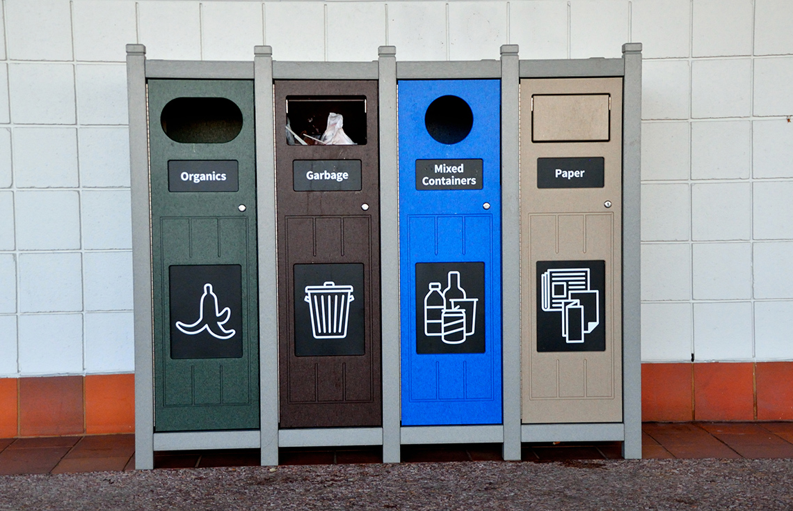 A row of trash bins including an organics bin, a garbage bin, a mixed containers bin and a paper bin.