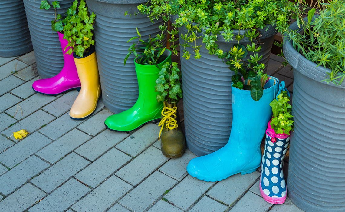Rubber boots and planters one after the other lined up. They all have plants in them.