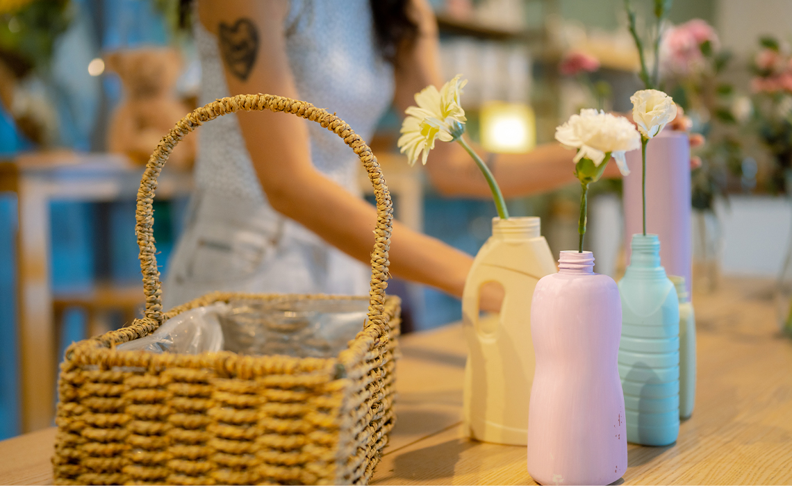 There is a basket on a table along with four different sized vases. The vases are   made from plastic bottles.