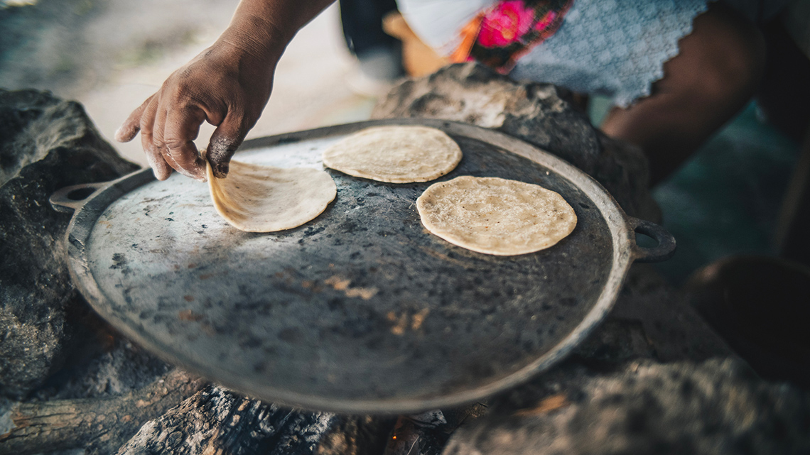 A person baking tortilla bread over a fire. 