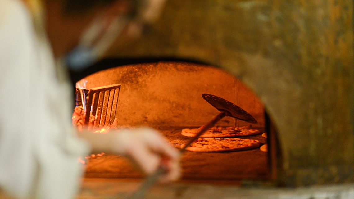 A person turning a pizza in a large pizza oven.