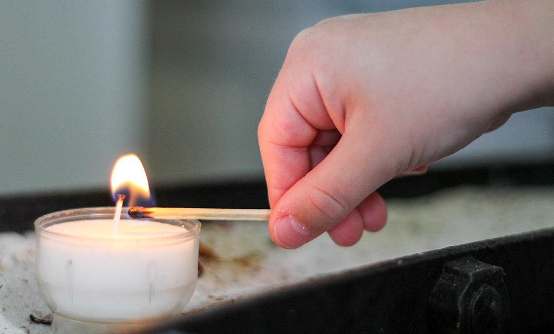 A hand holding a match next to a lit candle.