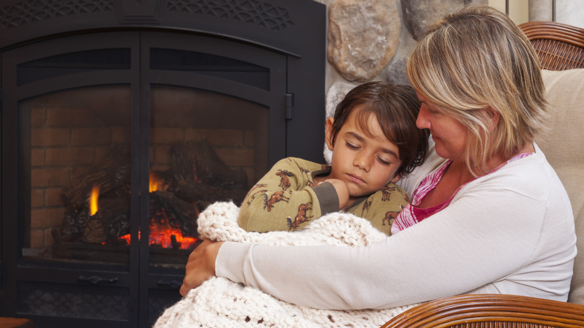 An adult and a child sitting together by a fireplace. 