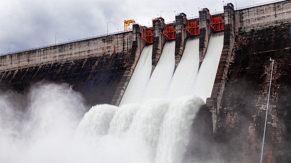 There is water rushing through channels that were created in a concrete wall. The water reaches a pool below.