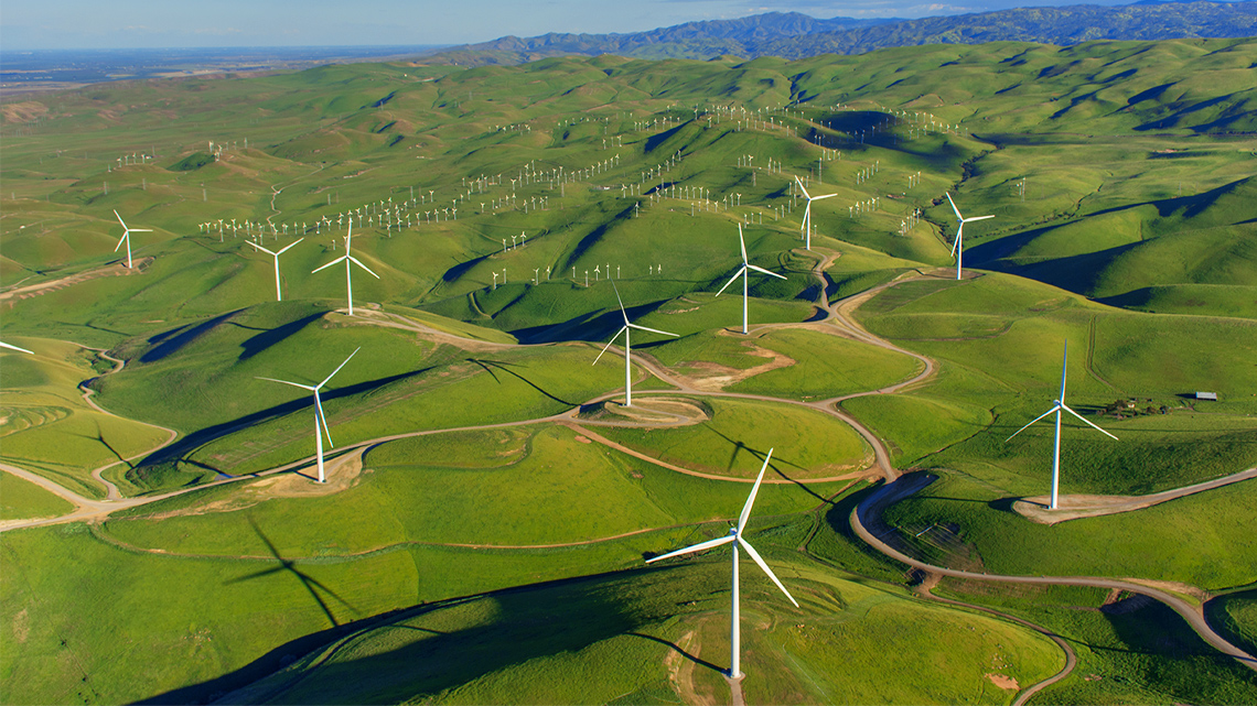There is a series of wind turbines in a large hilly field. There are many turbines throughout the hills.