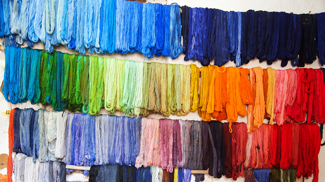 There are many fabrics hanging on a wall of all different colours.