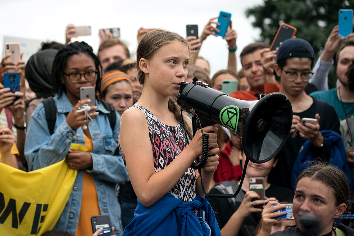 Greta Thunberg speaking into a megaphone, surrounded by a crowd