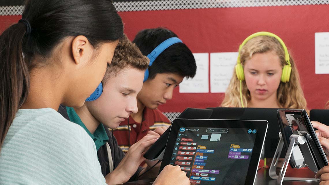 Four students using technology, and three are wearing headphones.