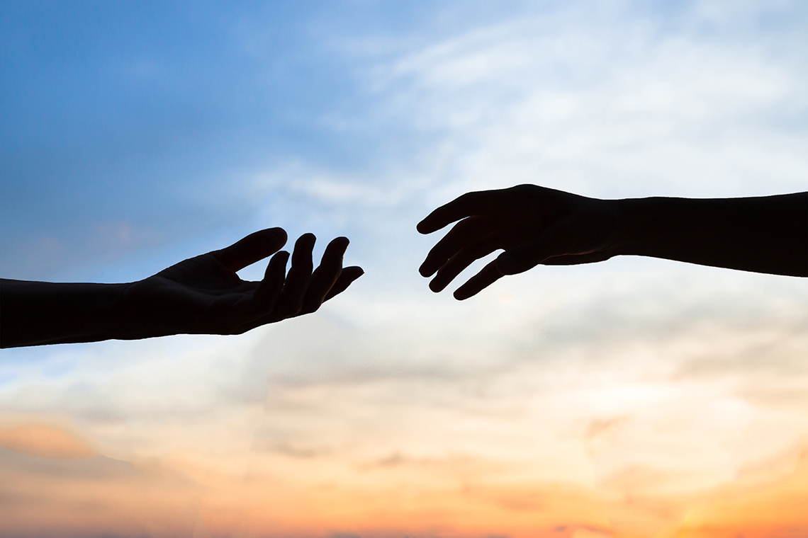 Silhouette of two hands reaching towards each other against a sky background.