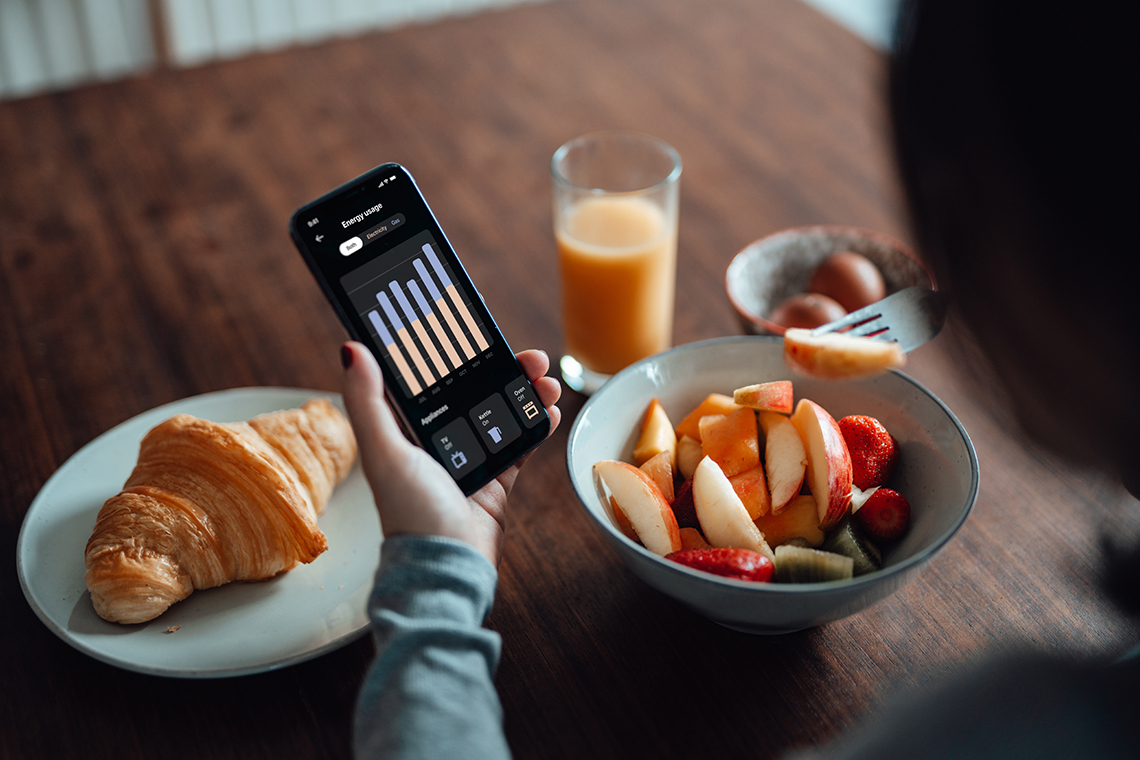 Energy usage A person looking at their energy usage app on their phone while eating some fruit.