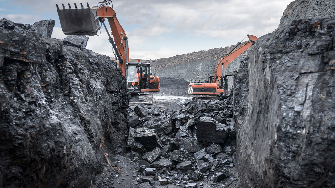 Two excavators digging out pieces of rock and dirt from a mine.