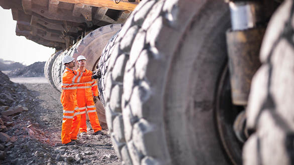 Two people standing beside a dump truck, the tires are taller than the people.