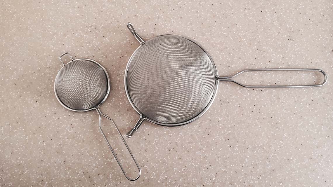 A small and a large strainer sitting on a kitchen counter.
