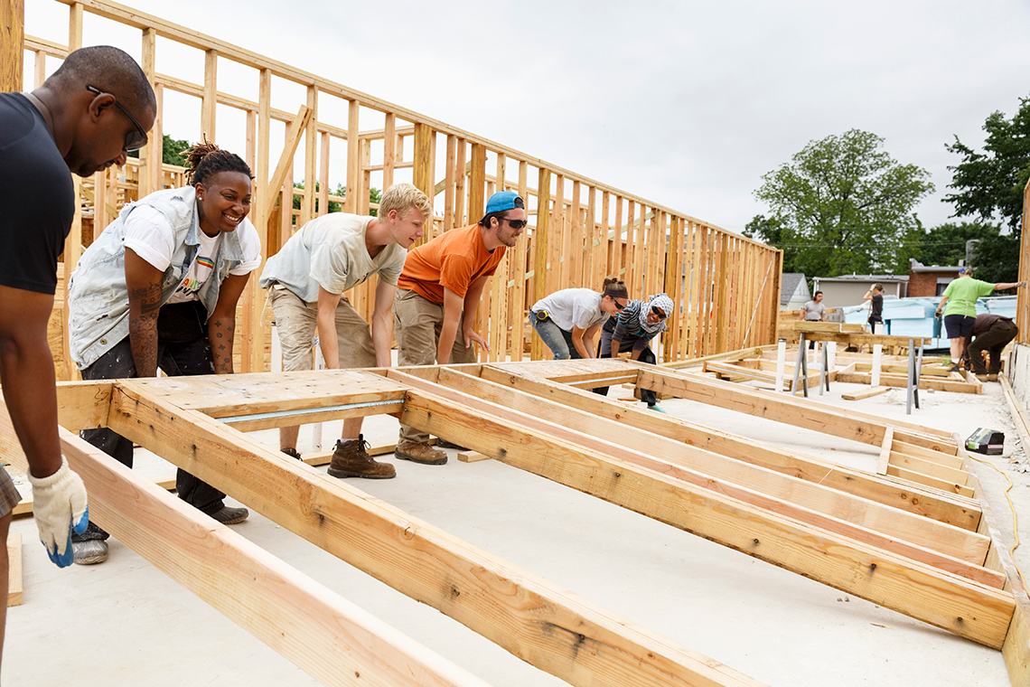 A group of people lifting up the framing of a house.