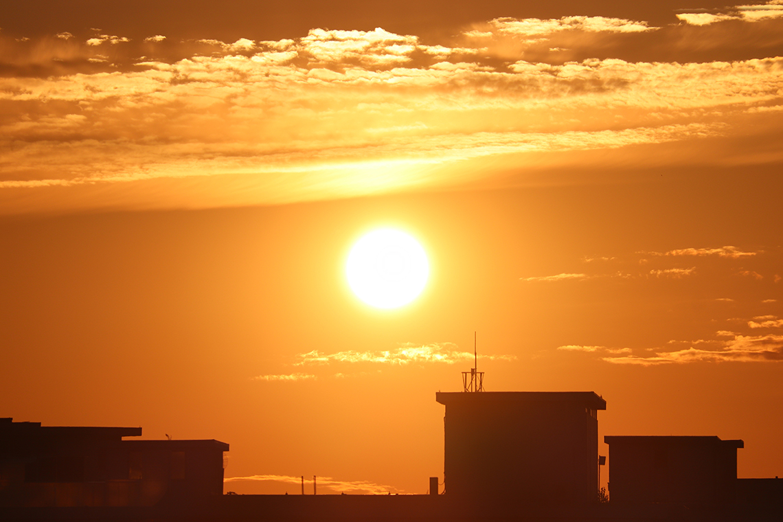 The sun shining in the sky over top of buildings.