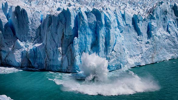 A piece of a melting glacier splashes as it falls into the ocean.