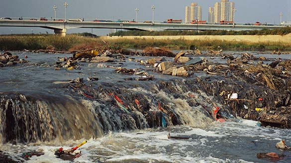 A polluted body of water with a highway and factories in the background.
