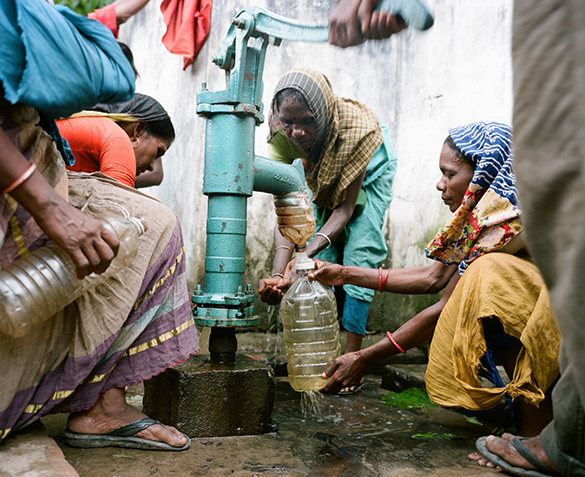A group of people using a home made water purification device to fill up their water bottles at a hand pump.