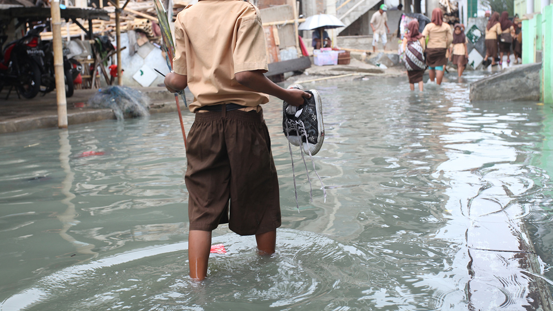 People walking through knee-deep water in a flooded urban area.