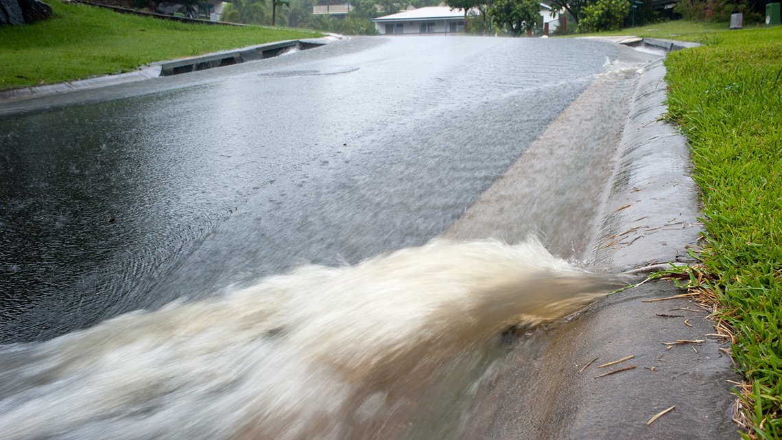 A closeup view of a street curb with grass and fast-moving rain runoff.