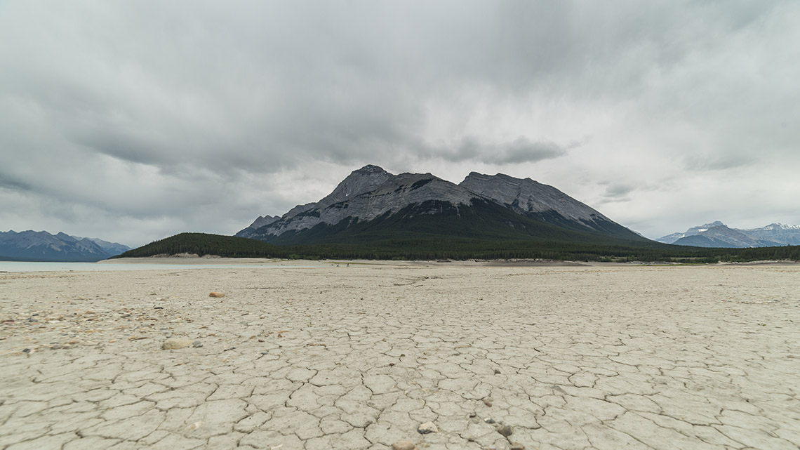 Dry and cracked ground with a mountain in the background and a cloud covered sky.