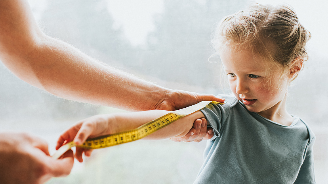 A child measuring their arm with the help of an adult.