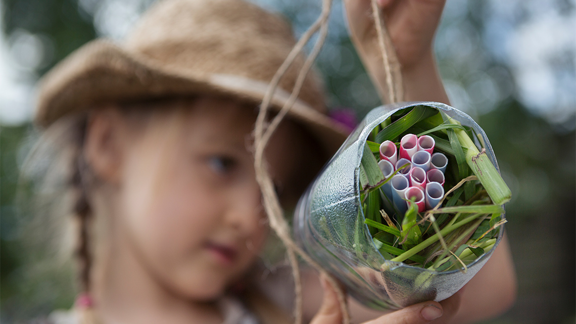 A person hanging up a bottle filled with leaves and straws.