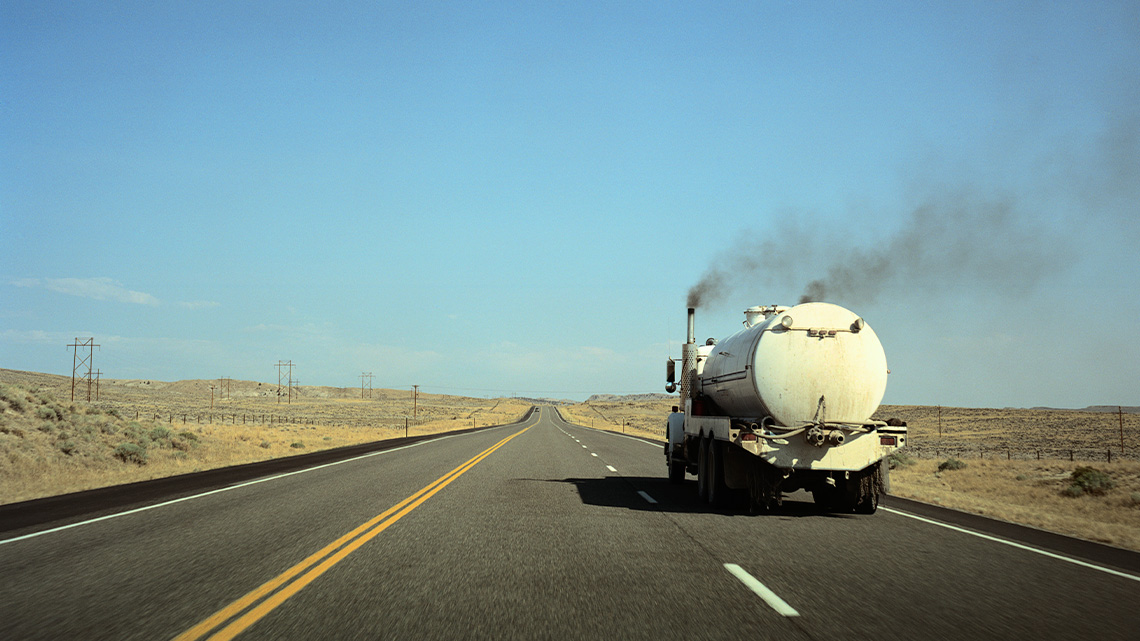 A large tanker truck on a road. There is exhaust coming from both of its exhaust pipes.