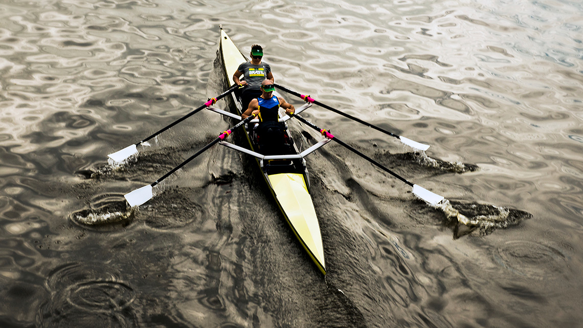 A rowing team using their oars to push water backwards and push their boat forwards.