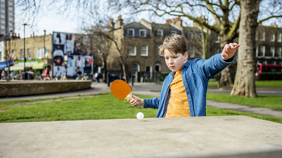 A learner uses a small hand paddle to hit a table tennis ball across the table.