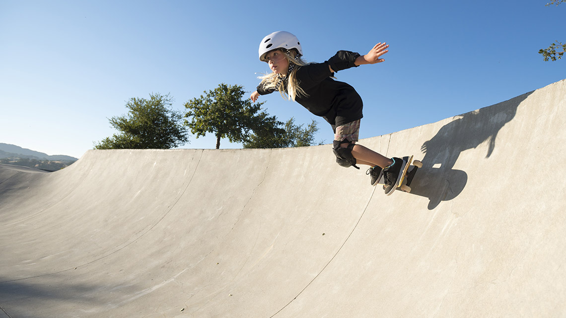 Child skateboarding A young person skateboards down a curved surface. They are wearing knee pads, elbow pads, and a helmet.