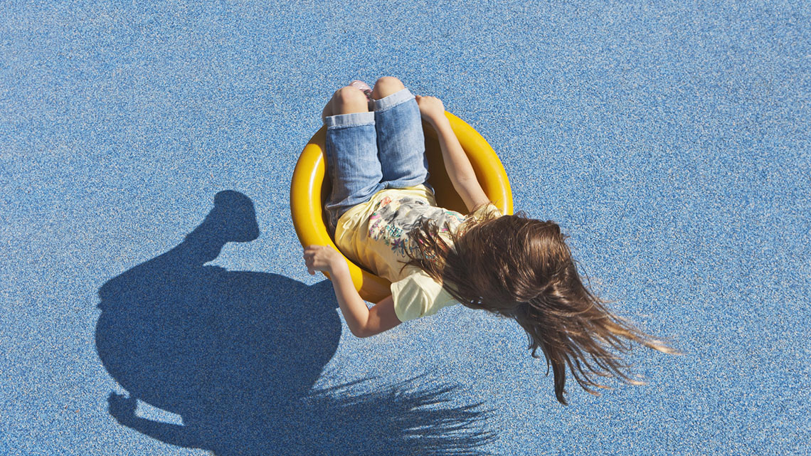 A child sits in a saddle spinner at a playground and spins around in a circle.