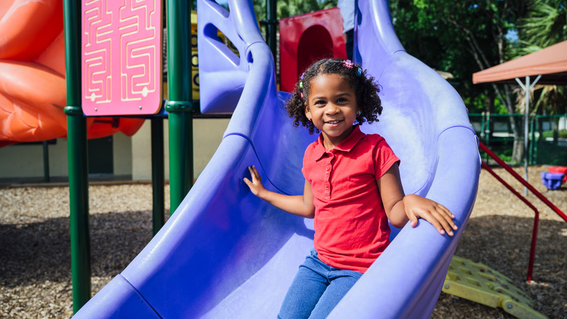 A child is half-way down a slide that is part of a playground structure.