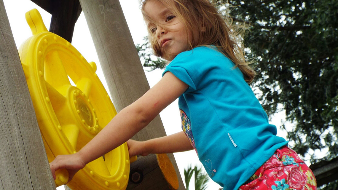 A child turns a large steering wheel that is part of a playground structure. 