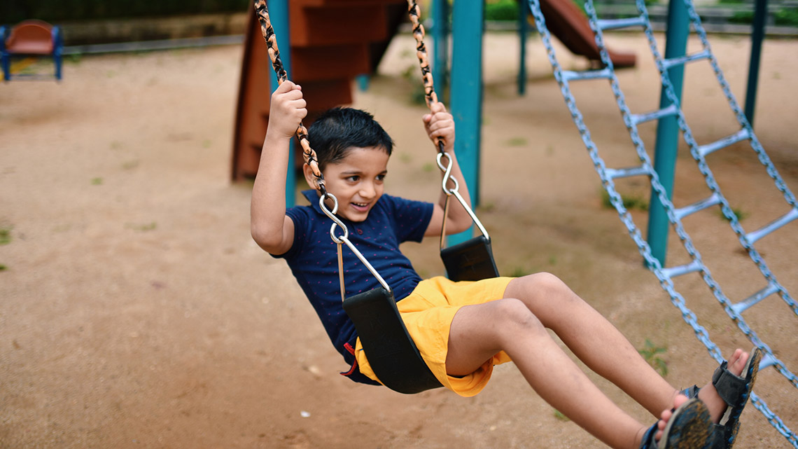 A child is sitting and moving on a swing. The swing is part of a playground structure.