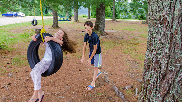 One learner is pushing another learner who is sitting on a tire swing.