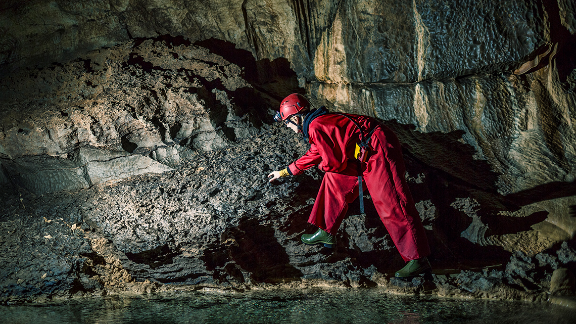 A geologist wearing a head lamp and special clothes explores a cave.