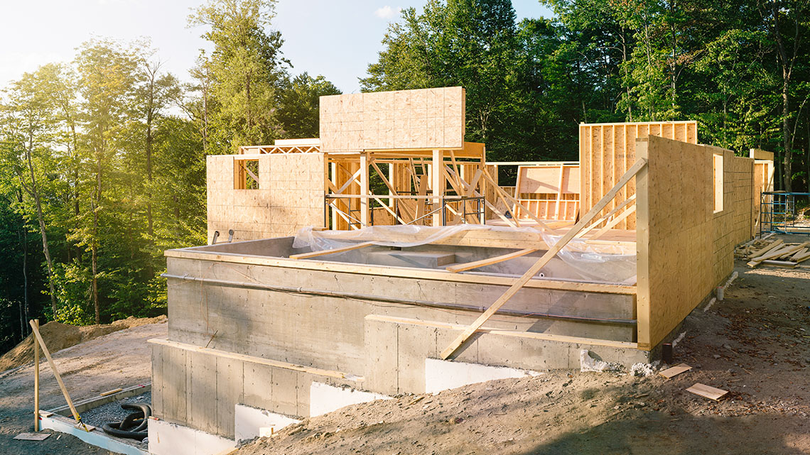 The concrete foundation of a house with wooden framing being constructed on top.