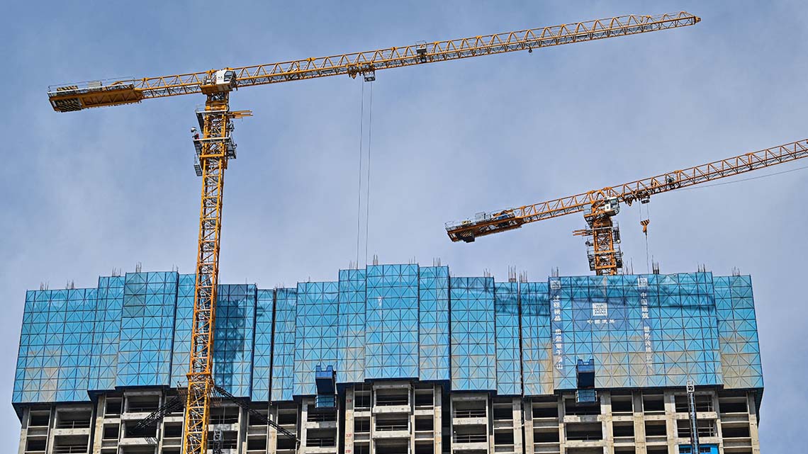 Two large cranes standing over a glass skyscraper under construction.