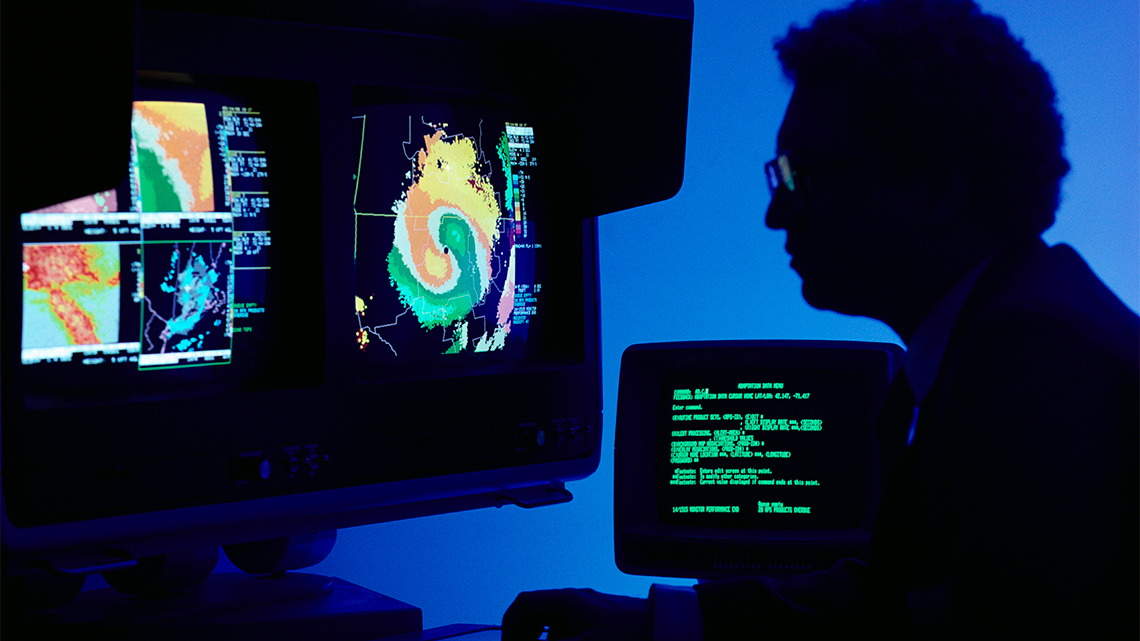 A person examines several computer screens with weather information on them.
