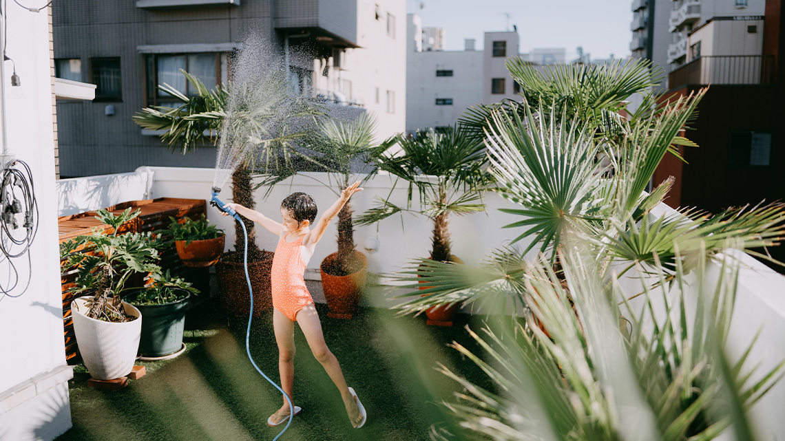 A person waters potted plants in a rooftop garden.