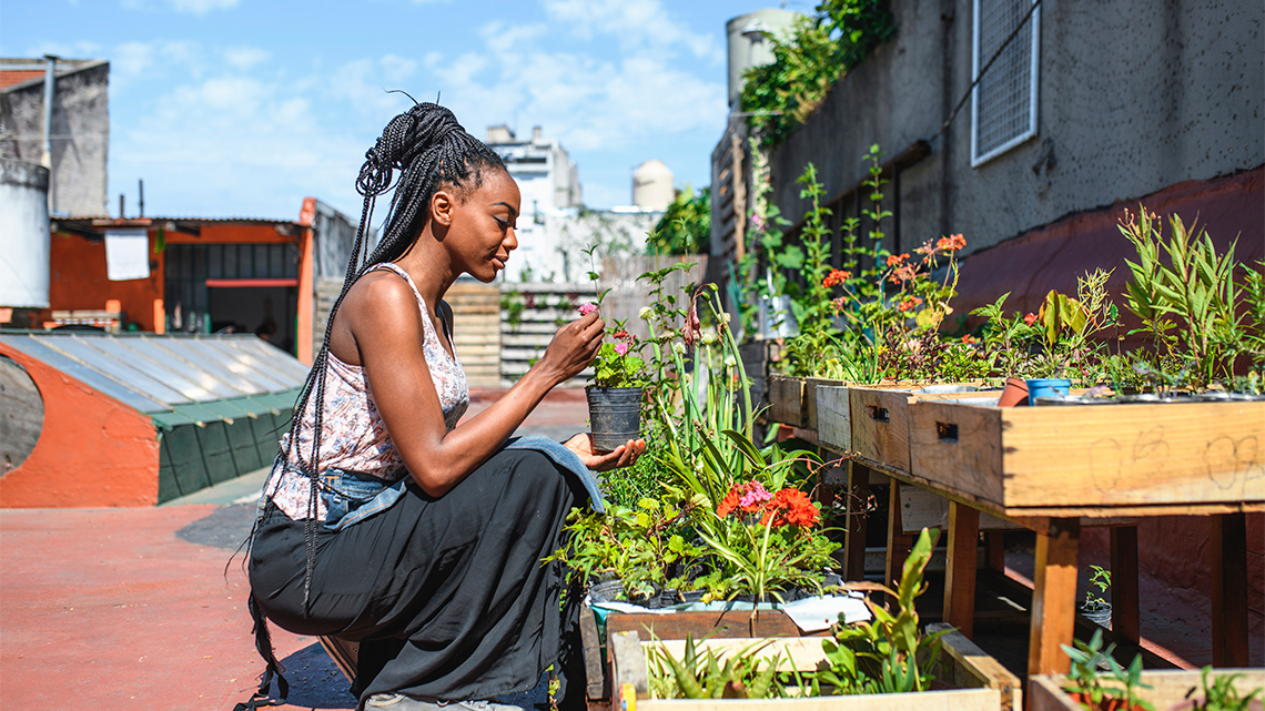 A person checks on their plants in a small area of a rooftop.