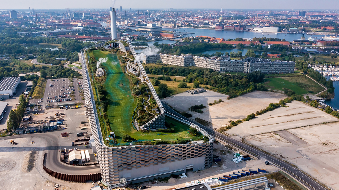 An industrial building has a green roof next to its smoke stacks.