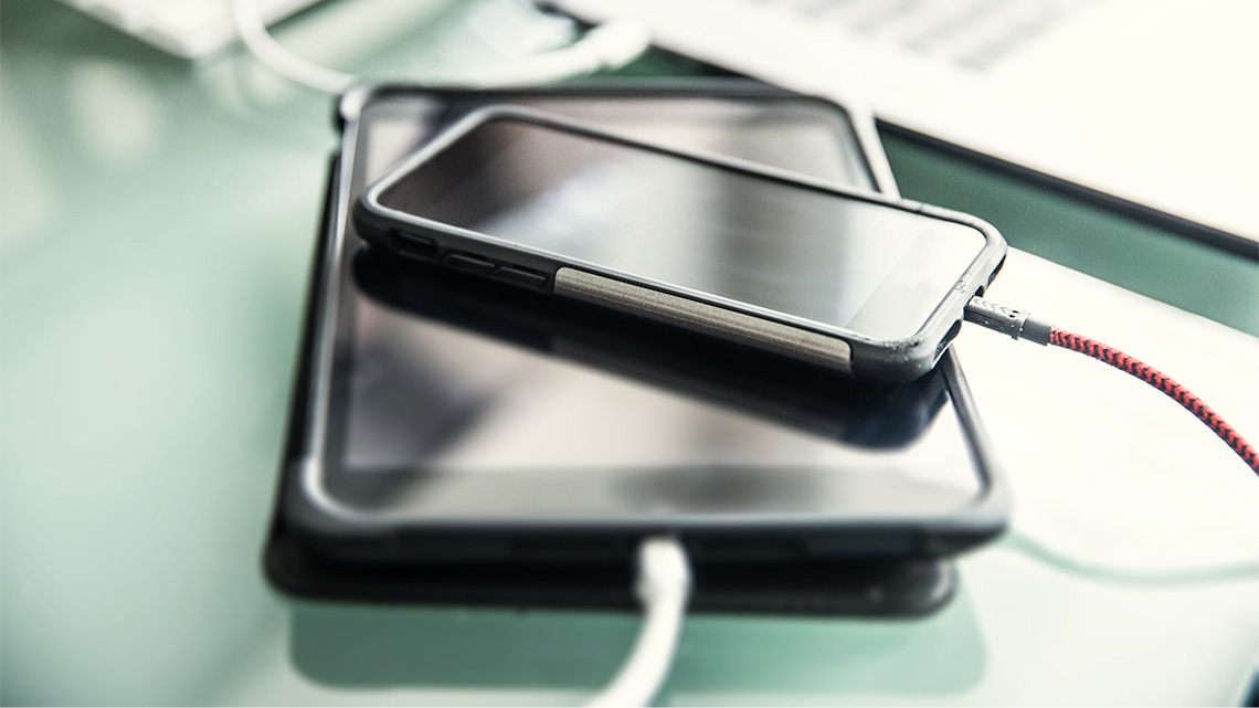 A smartphone and a tablet stacked on one another being charged with power cords plugged into each one.