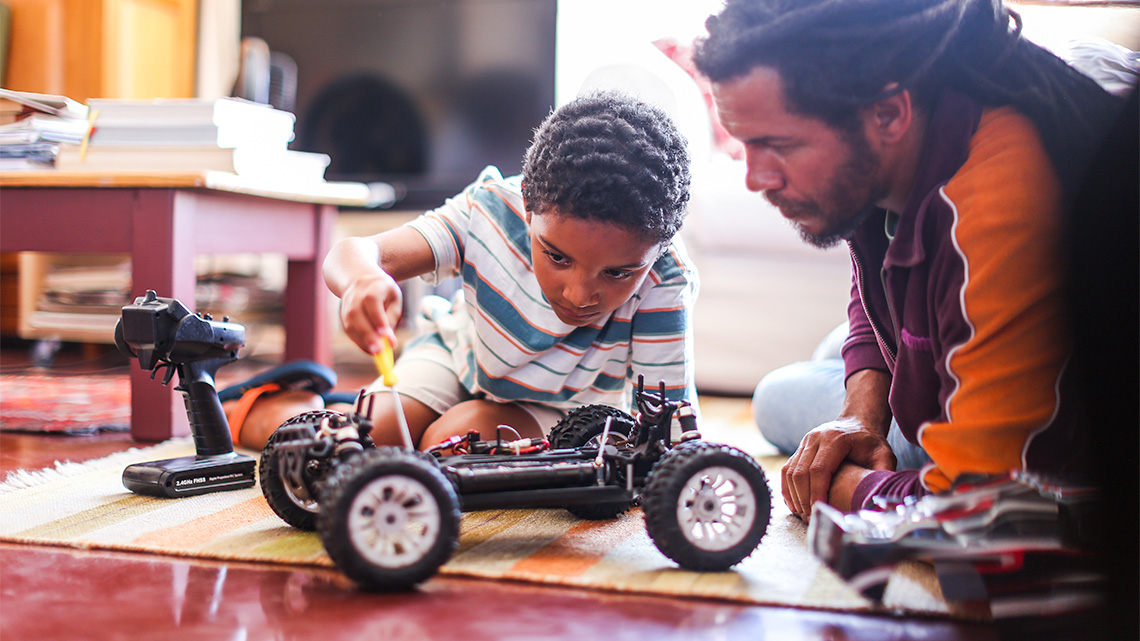 An adult and child repairing a remote-controlled toy car using a screwdriver.