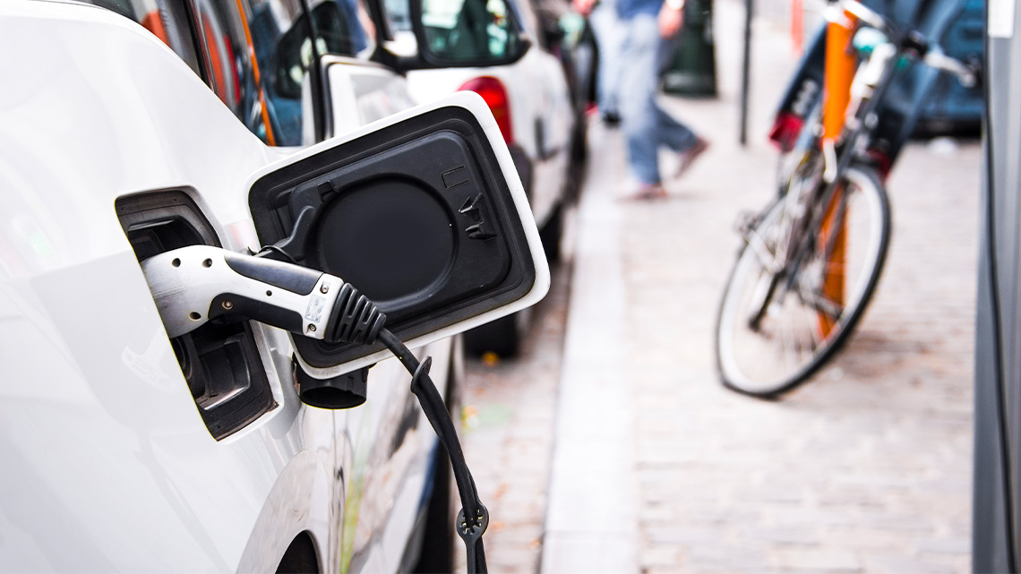 An electric car parked and plugged into a charging station on a busy city street.